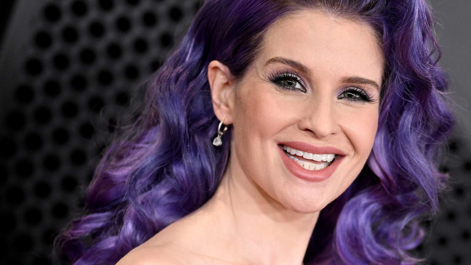 Kelly Osbourne with vibrant purple hair smiling at a red carpet event