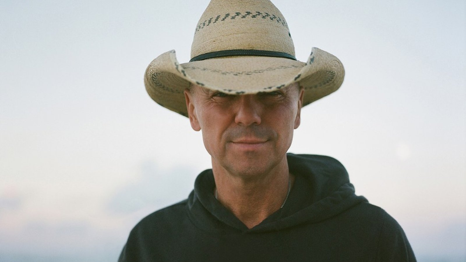 Country music singer Kenny Chesney wearing a straw cowboy hat against a bright background