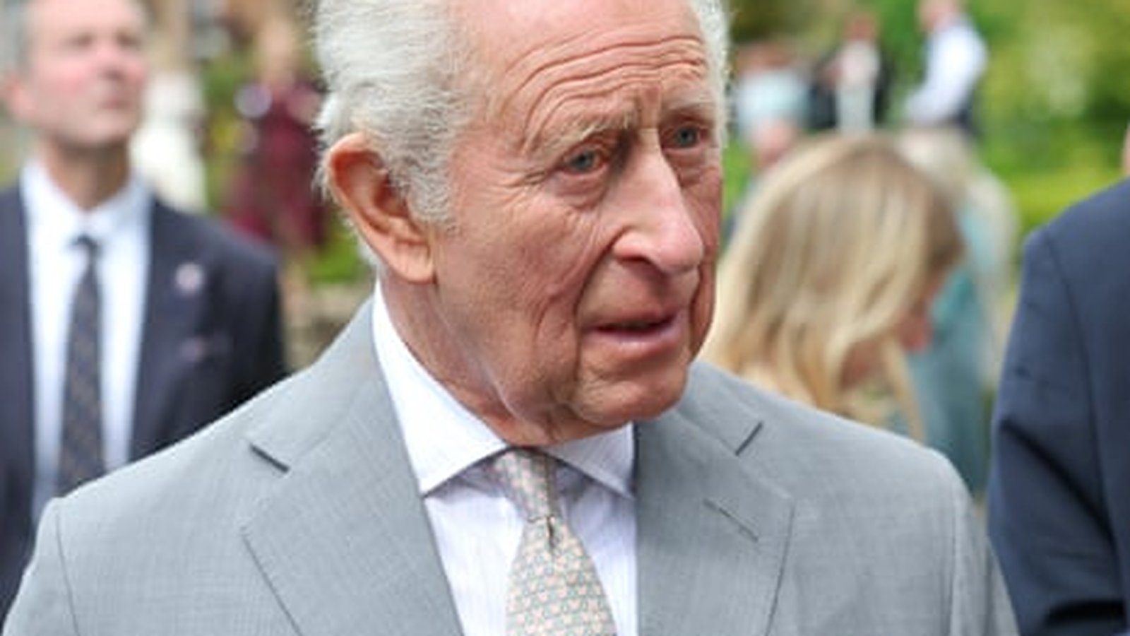 King Charles III wearing a grey suit and tie during a public appearance