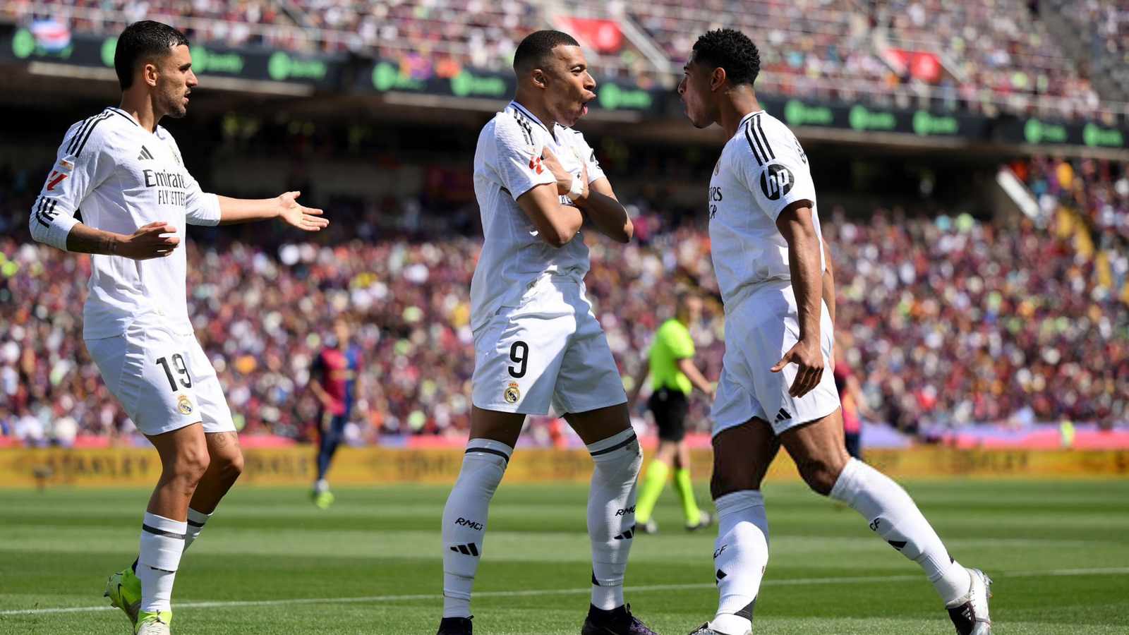 Kylian Mbappé celebrating a goal on the pitch with Real Madrid teammates in white kits