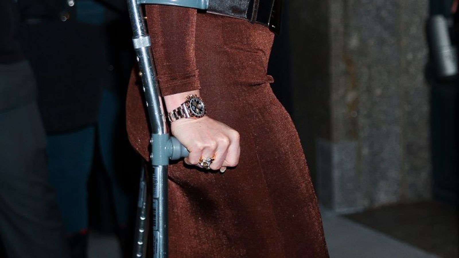 Lindsey Vonn smiling while walking with a forearm crutch in a brown dress