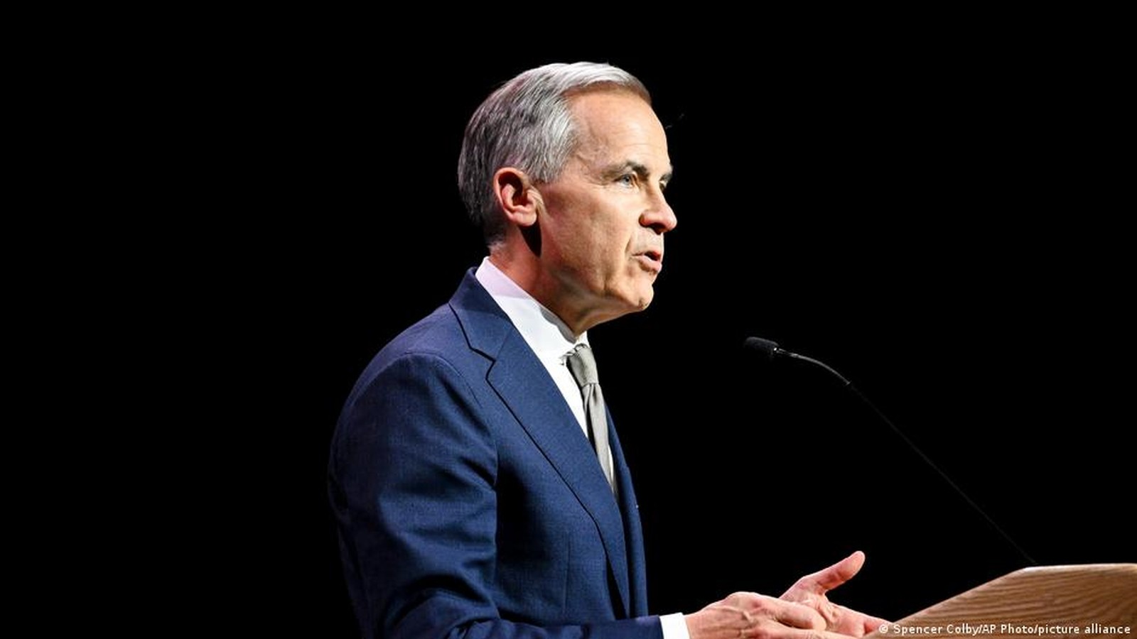 Mark Carney speaking at a podium against a dark background during a summit