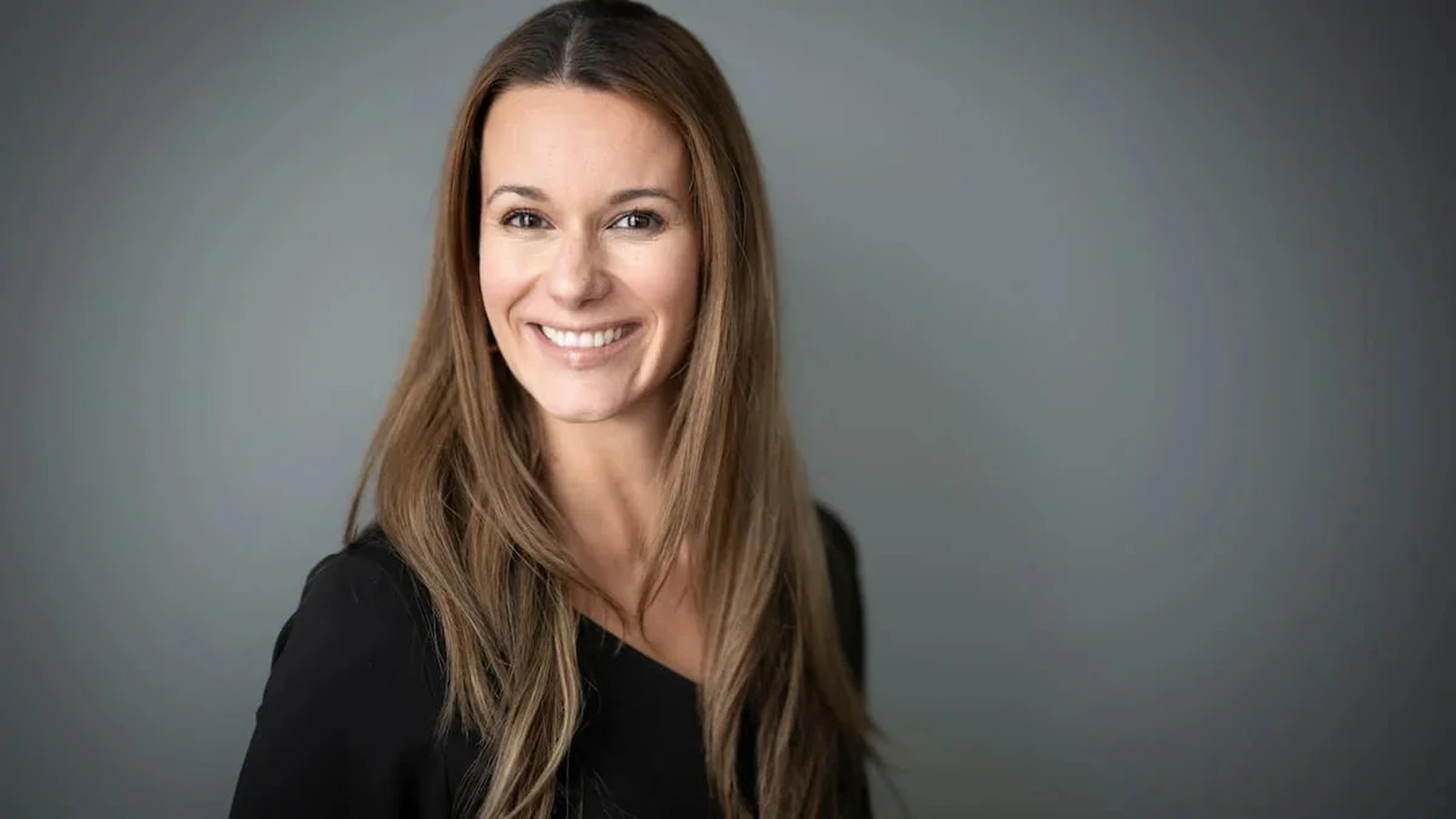 Journalist Monic Neron smiling at the camera against a plain grey background