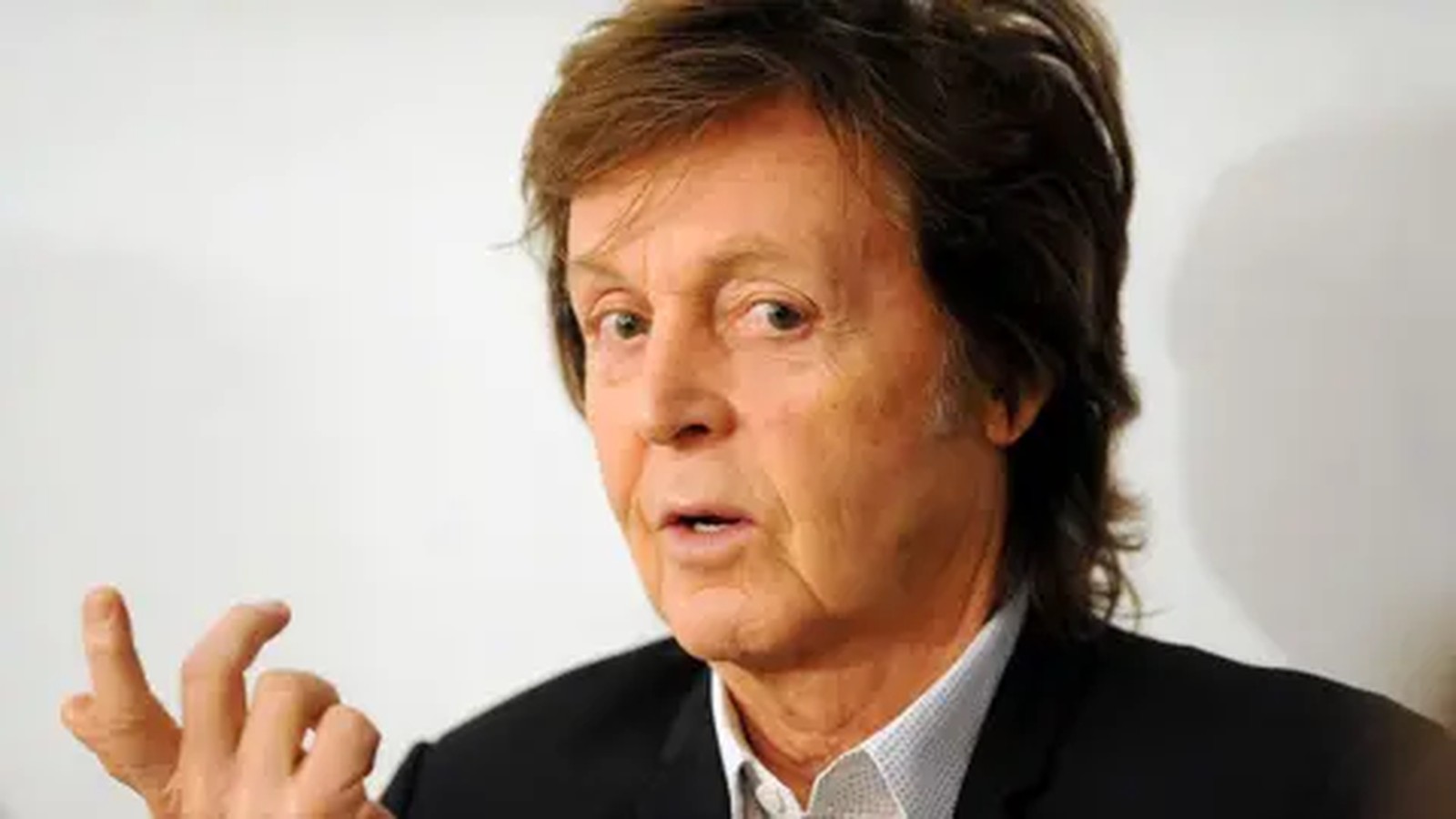 A close up portrait of musician Paul McCartney speaking against a white background
