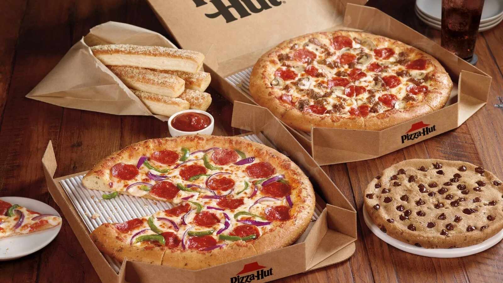 A Pizza Hut meal featuring two pizzas, breadsticks, dipping sauce, and a chocolate chip cookie