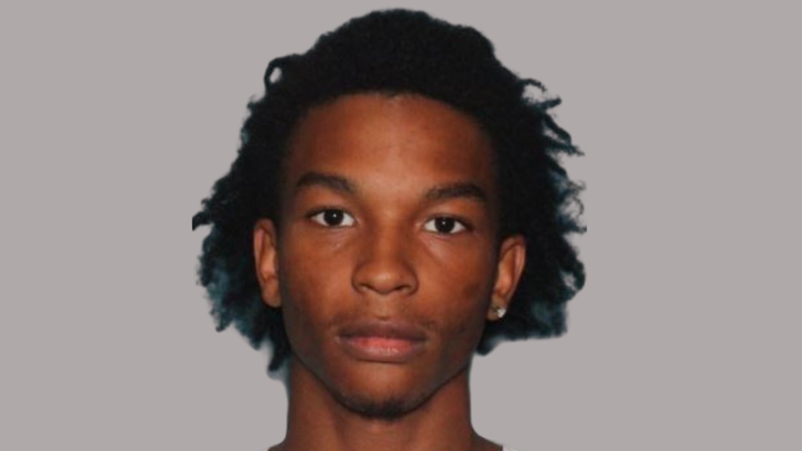 A young man with dark curly hair posing for a police mugshot portrait