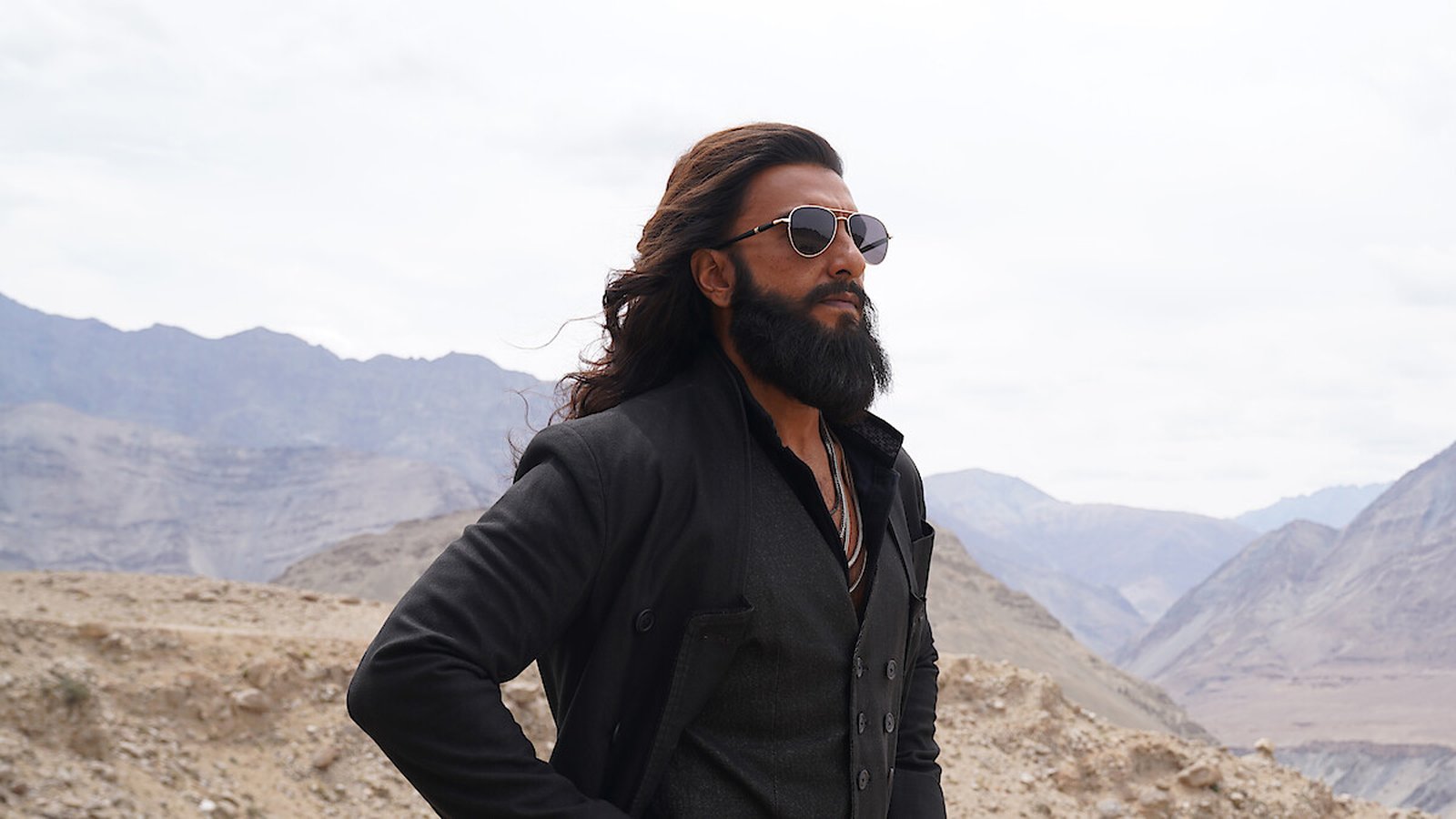 Ranveer Singh with long hair and beard wearing sunglasses in a mountainous landscape