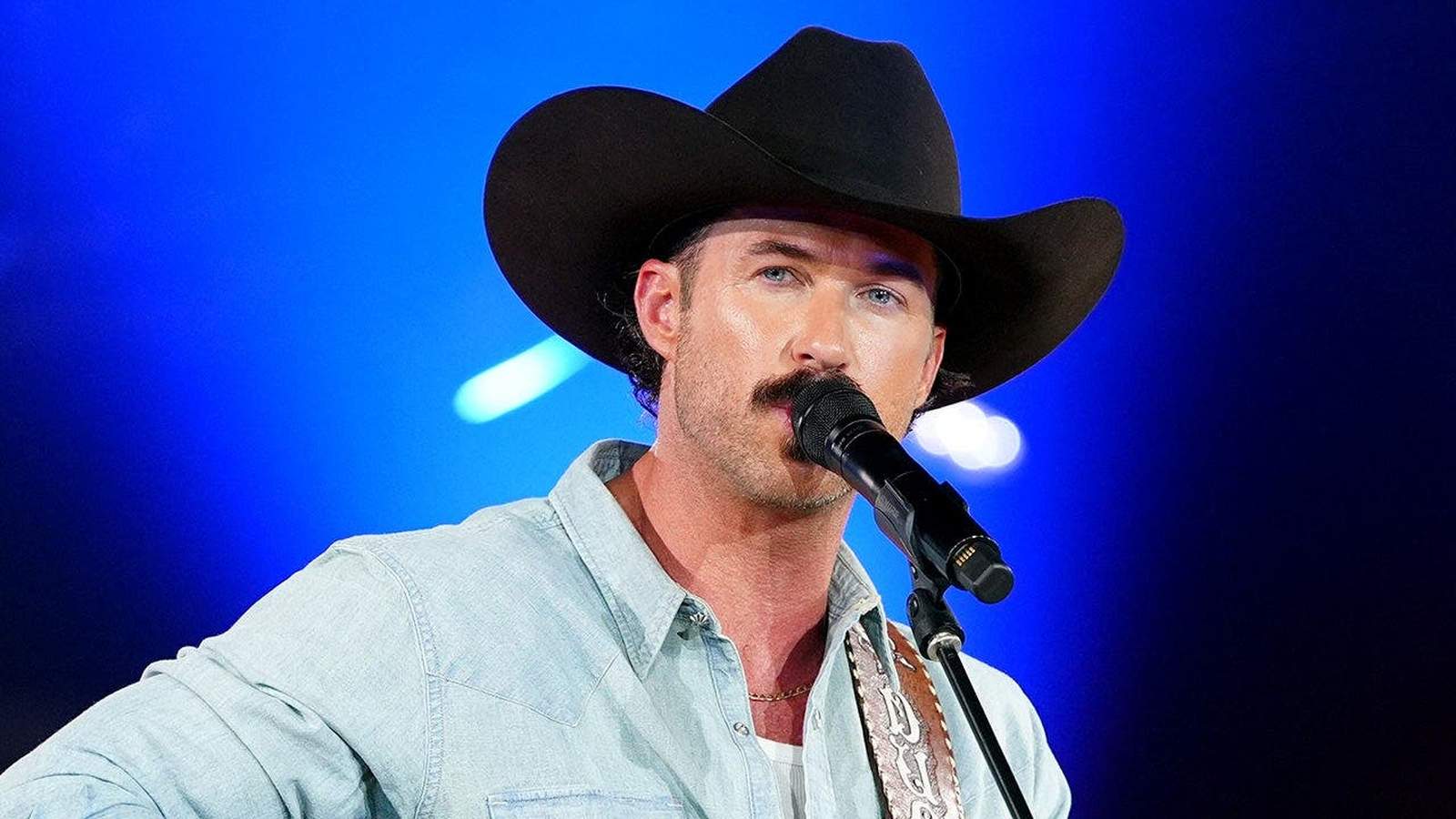 Country singer Riley Green wearing a cowboy hat performing into a microphone on stage