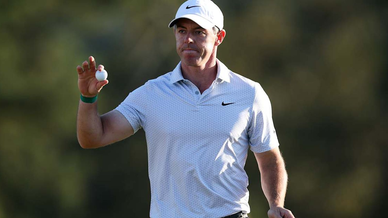 Golfer Rory McIlroy in white cap and light blue polo holding a golf ball