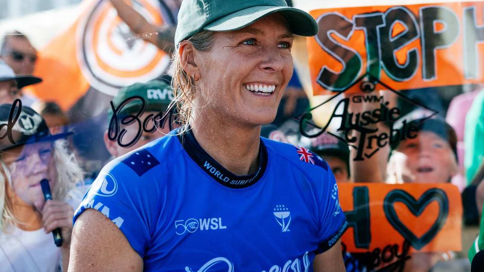 Professional surfer Stephanie Gilmore smiling while wearing a blue jersey and green cap
