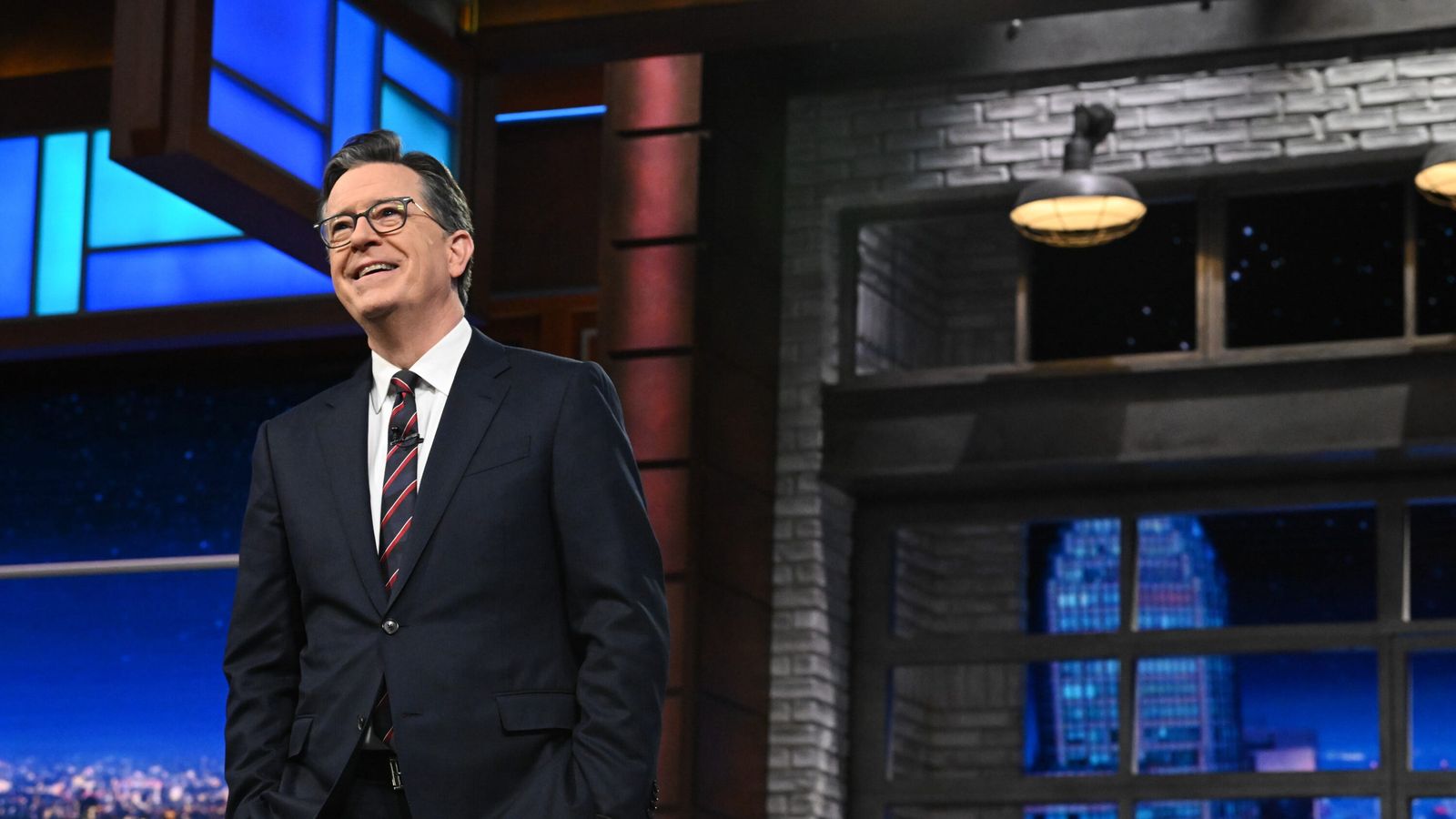 Stephen Colbert wearing a suit and glasses standing on the Late Show stage