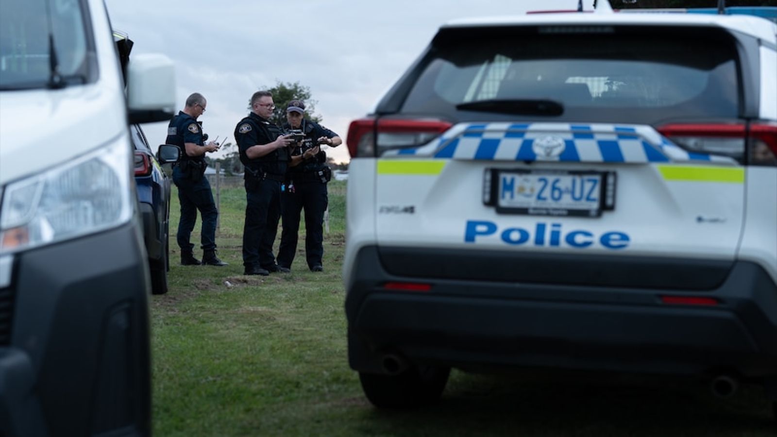 Tasmania police officers standing near a marked police vehicle at a crime scene