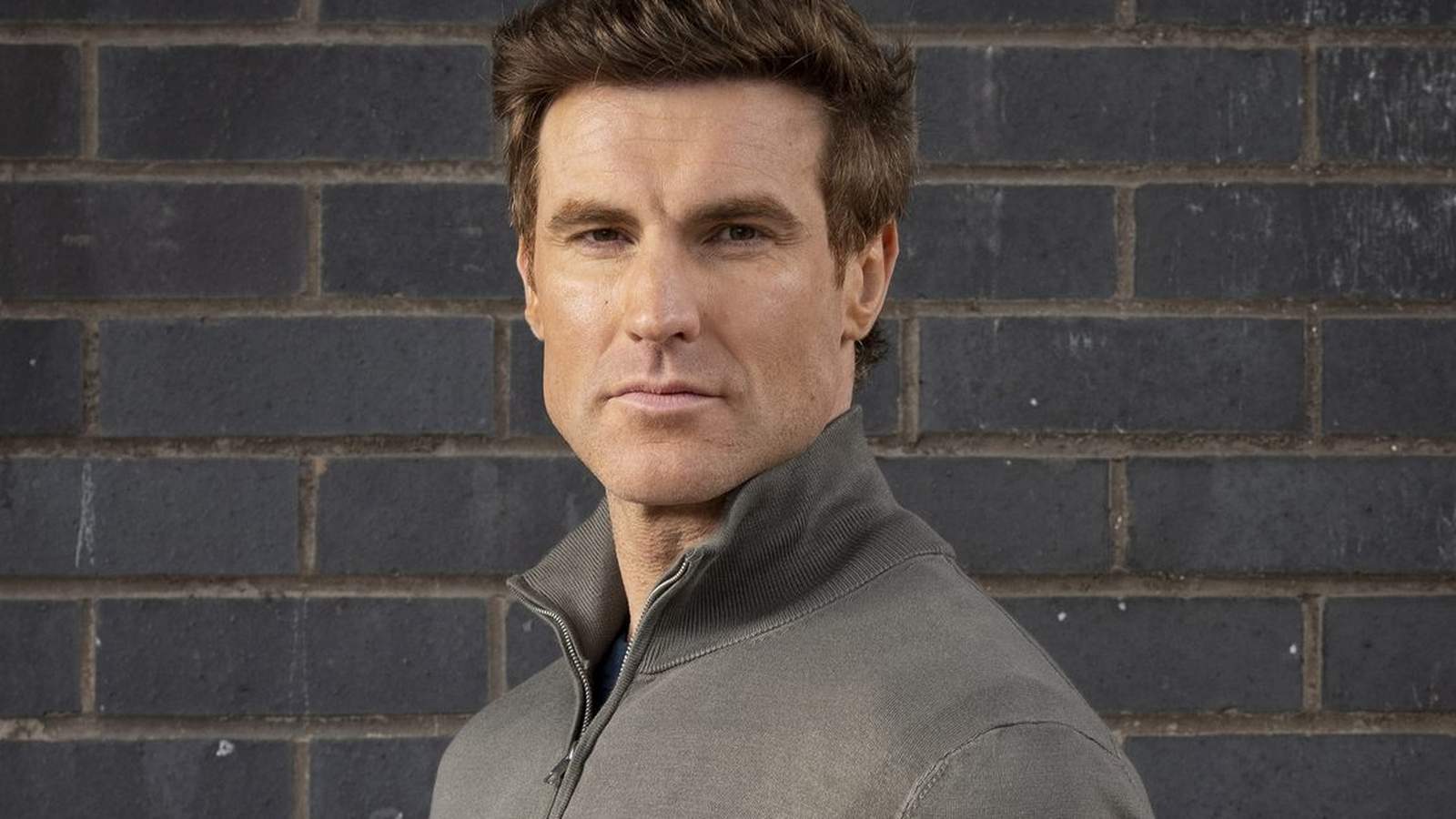 A close up portrait of a man with brown hair wearing a grey sweater