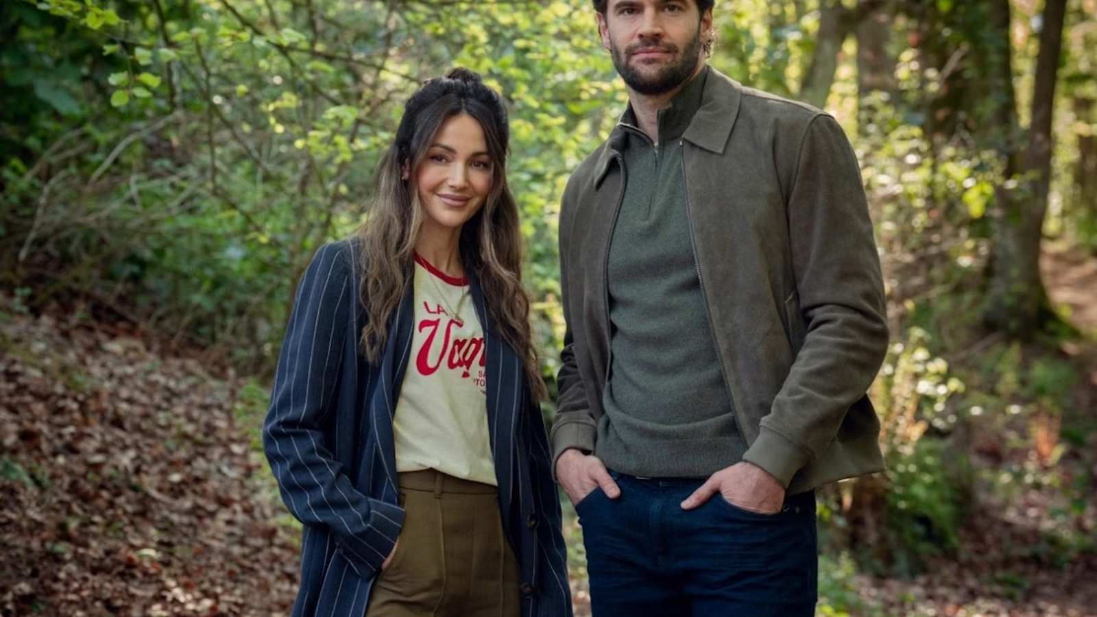 Tom Bateman and Michelle Keegan standing together in a lush green forest setting