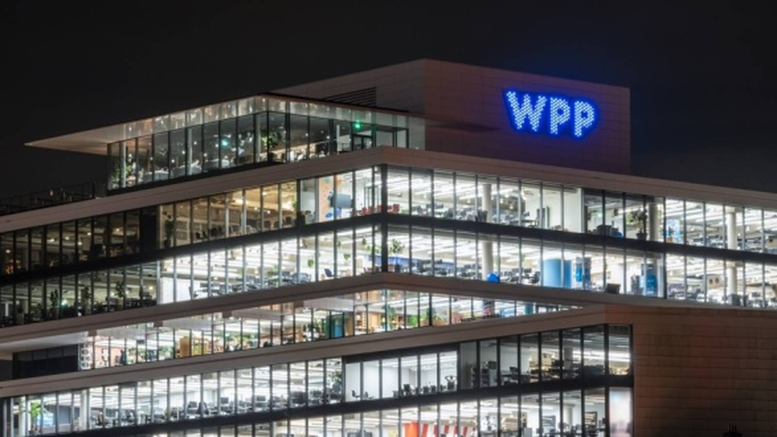 The illuminated WPP corporate headquarters building at night with visible office interior lighting