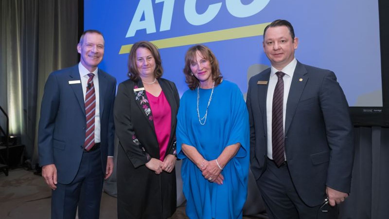 Four business professionals standing in front of a large blue ATCO company logo