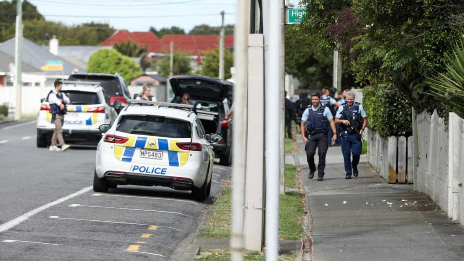 New Zealand police officers walking along a suburban street near parked patrol cars