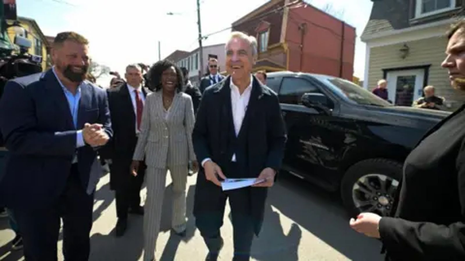 Mark Carney smiling while walking outdoors surrounded by campaign staff and supporters