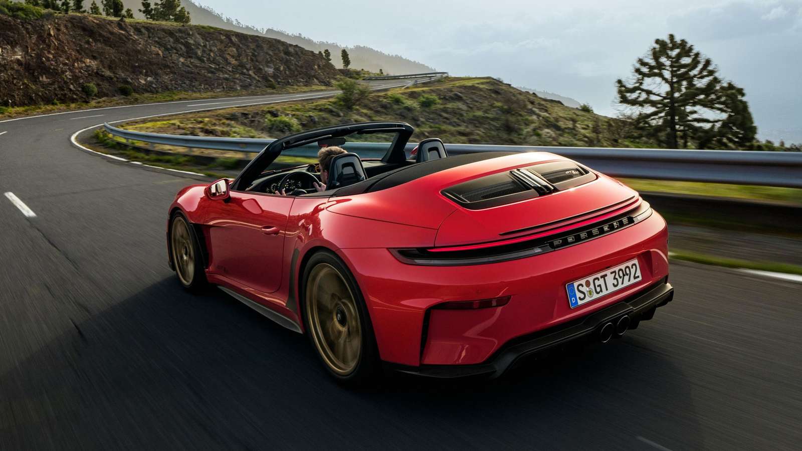 A red Porsche 911 GT3 SC convertible driving on a winding mountain road