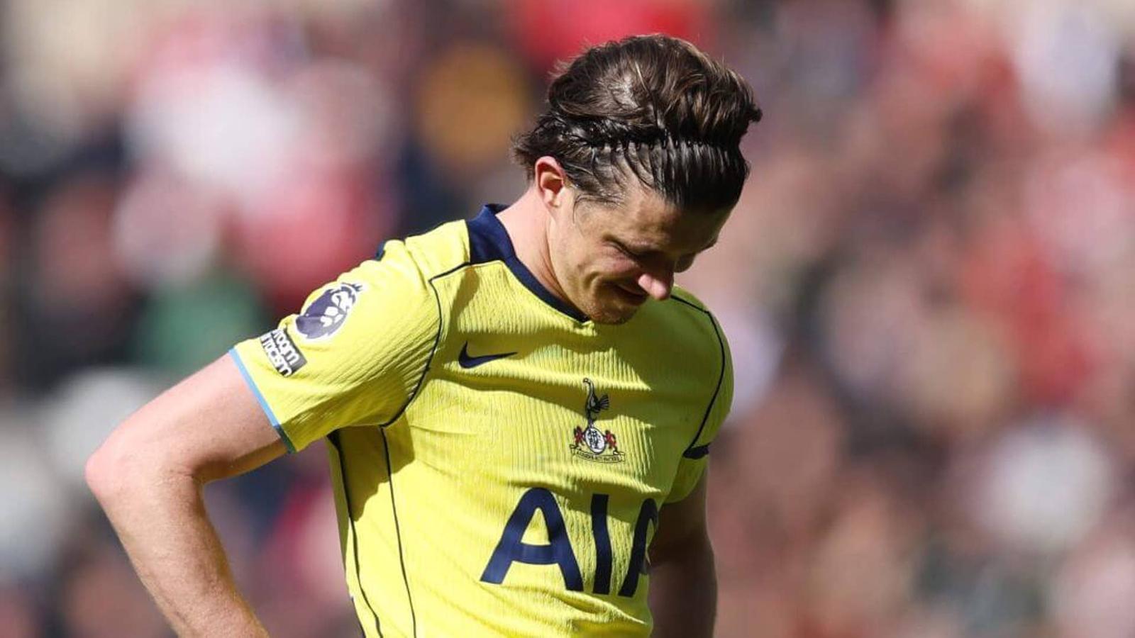 A dejected Tottenham Hotspur player in a yellow jersey looking down during a match