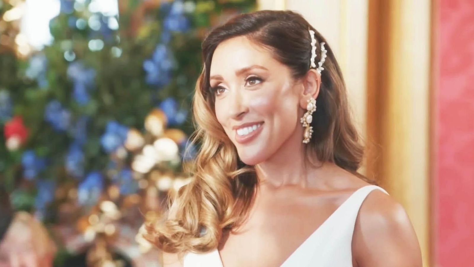A smiling woman with wavy hair wearing a white dress and pearl earrings