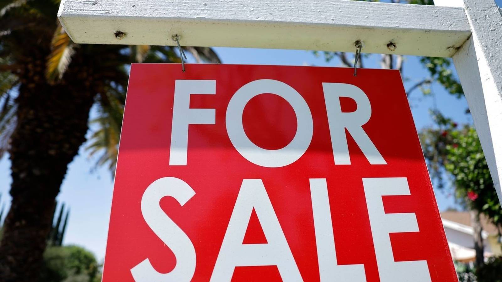 A bright red real estate for sale sign hanging from a white post