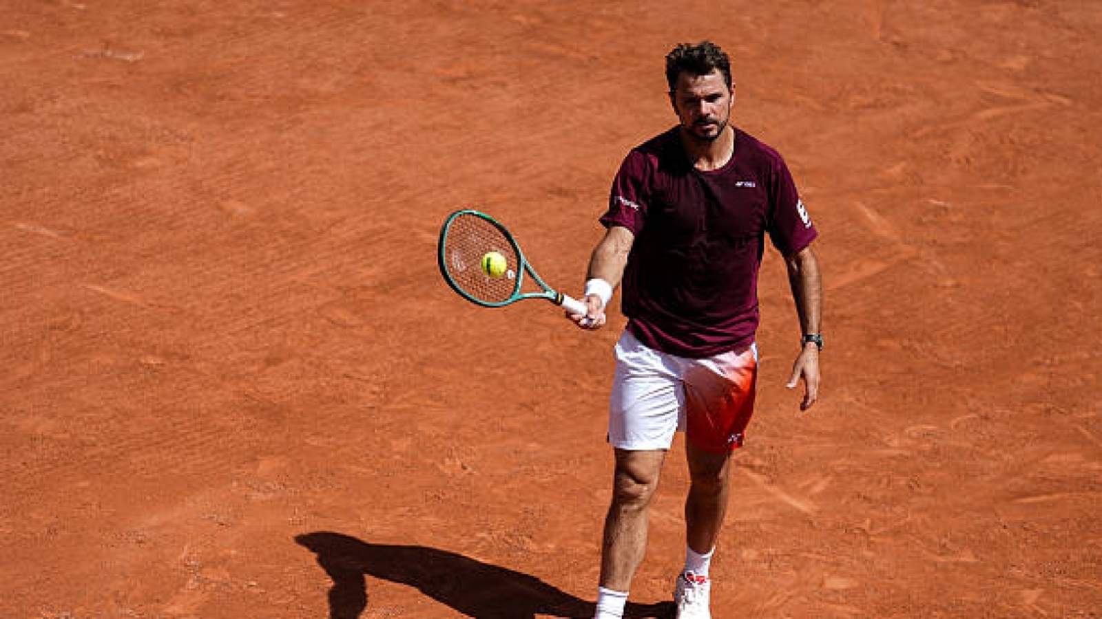 Stan Wawrinka holding a tennis racket on a red clay tennis court surface