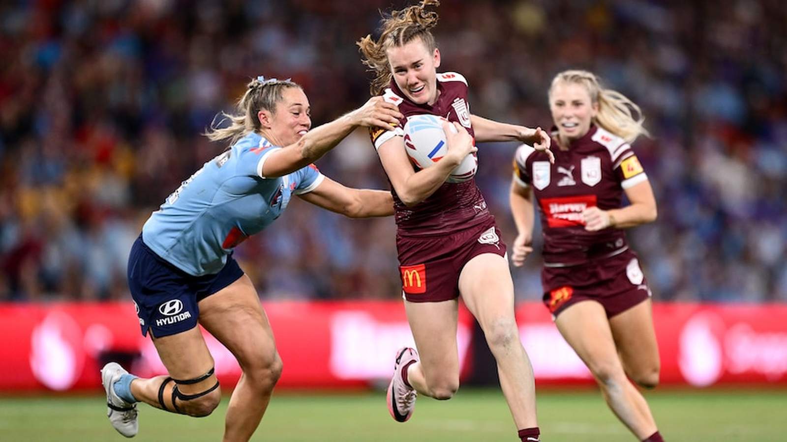 A Queensland player runs with the ball while a New South Wales player tackles