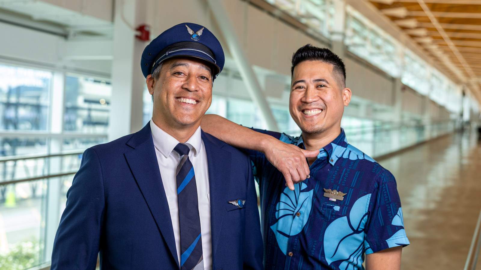 An Alaska Airlines pilot in uniform standing next to a smiling airline employee