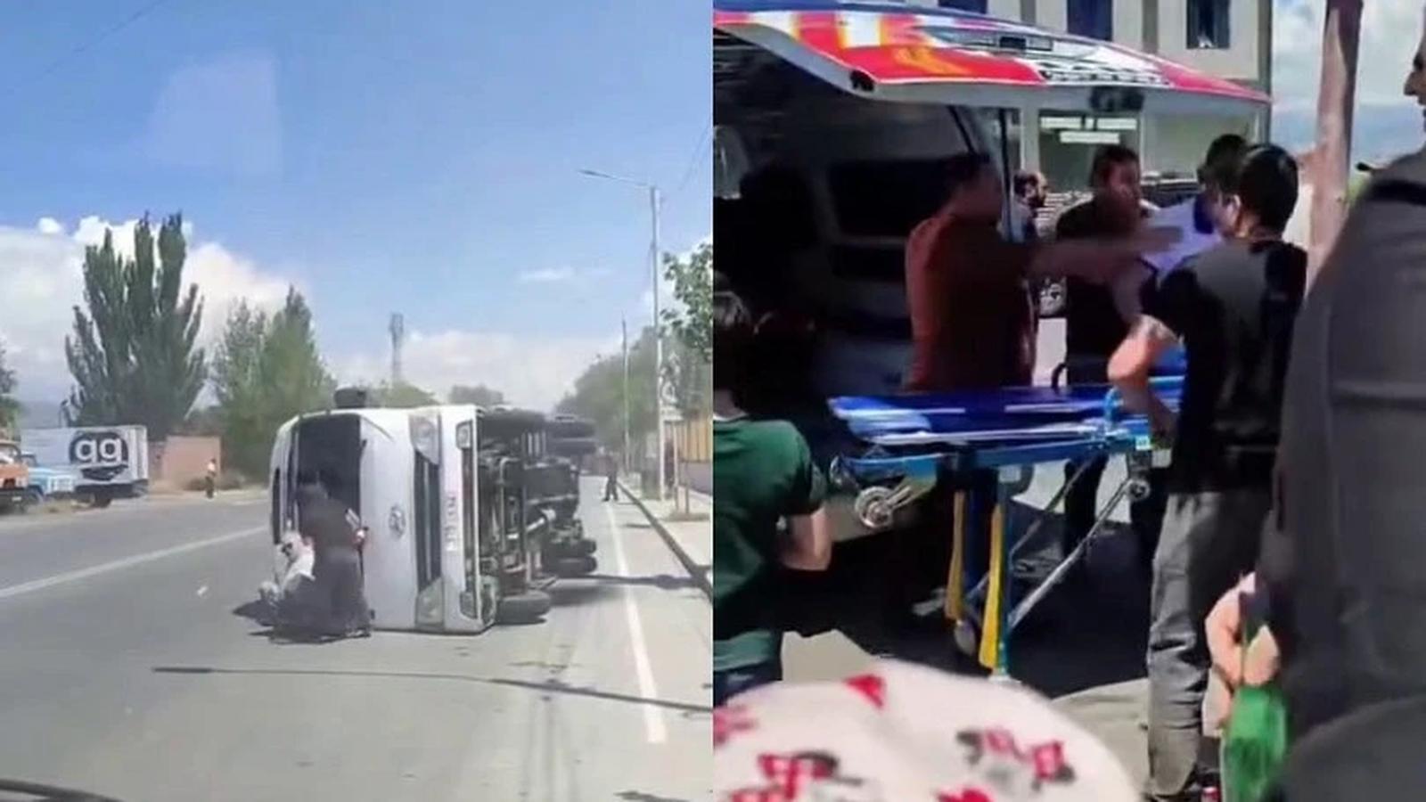 An overturned white bus on a road with emergency responders attending to victims