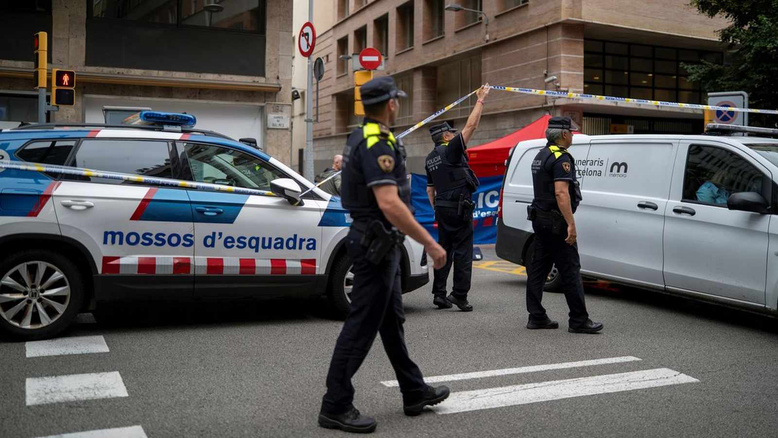 Mossos dEsquadra police officers securing a crime scene with tape on a Barcelona street