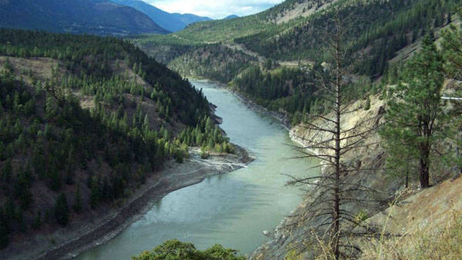 A winding river flows through a deep valley surrounded by forested mountains in British Columbia