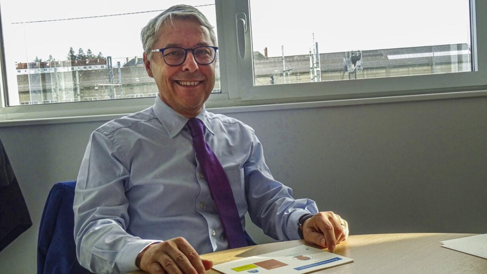 Claude Guillemot wearing a light blue shirt and purple tie smiling at camera