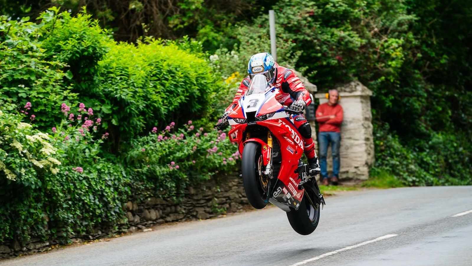 Dean Harrison riding a red Honda motorcycle performing a wheelie on a road