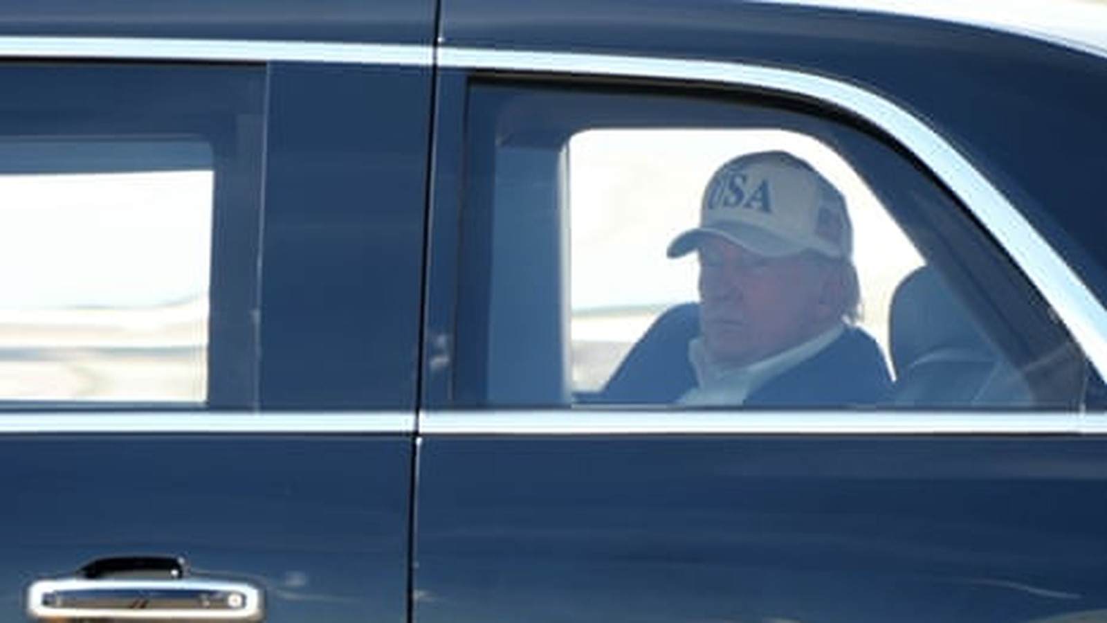 Donald Trump wearing a USA cap sitting in the back of a car