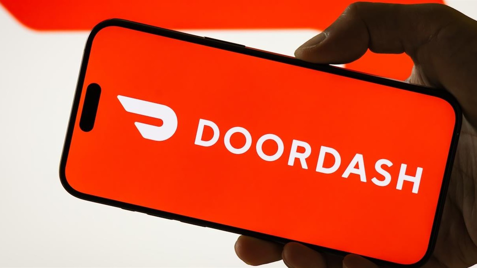 A hand holding a smartphone displaying the red DoorDash logo on the screen