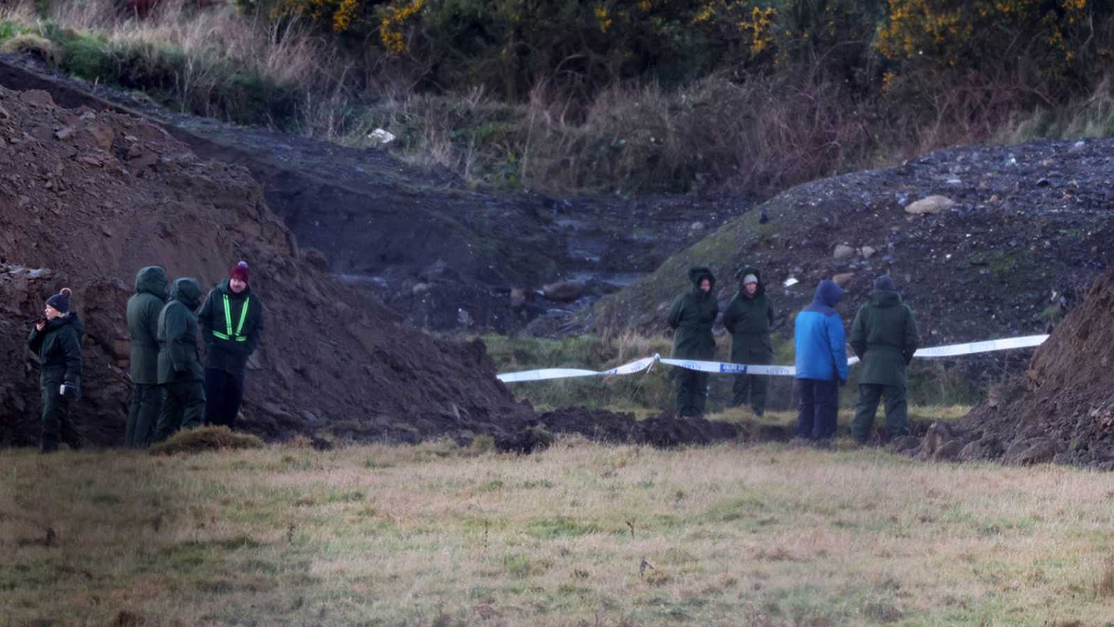 Gardaí in uniform standing near mounds of earth at a forensic search site