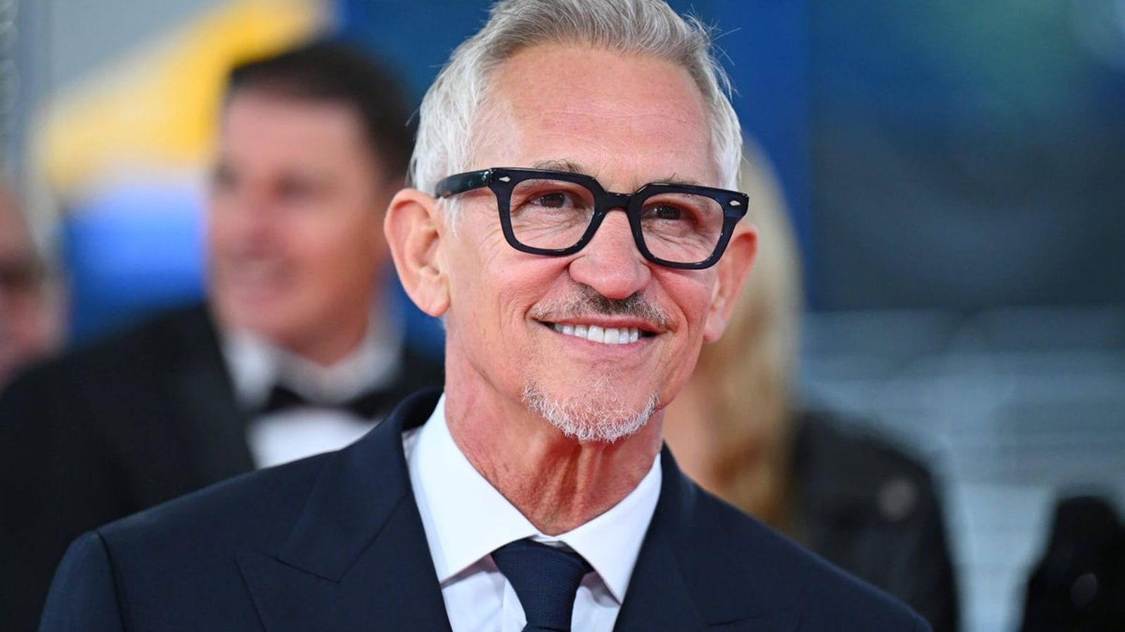 Gary Lineker wearing black framed glasses and a suit smiling at an event
