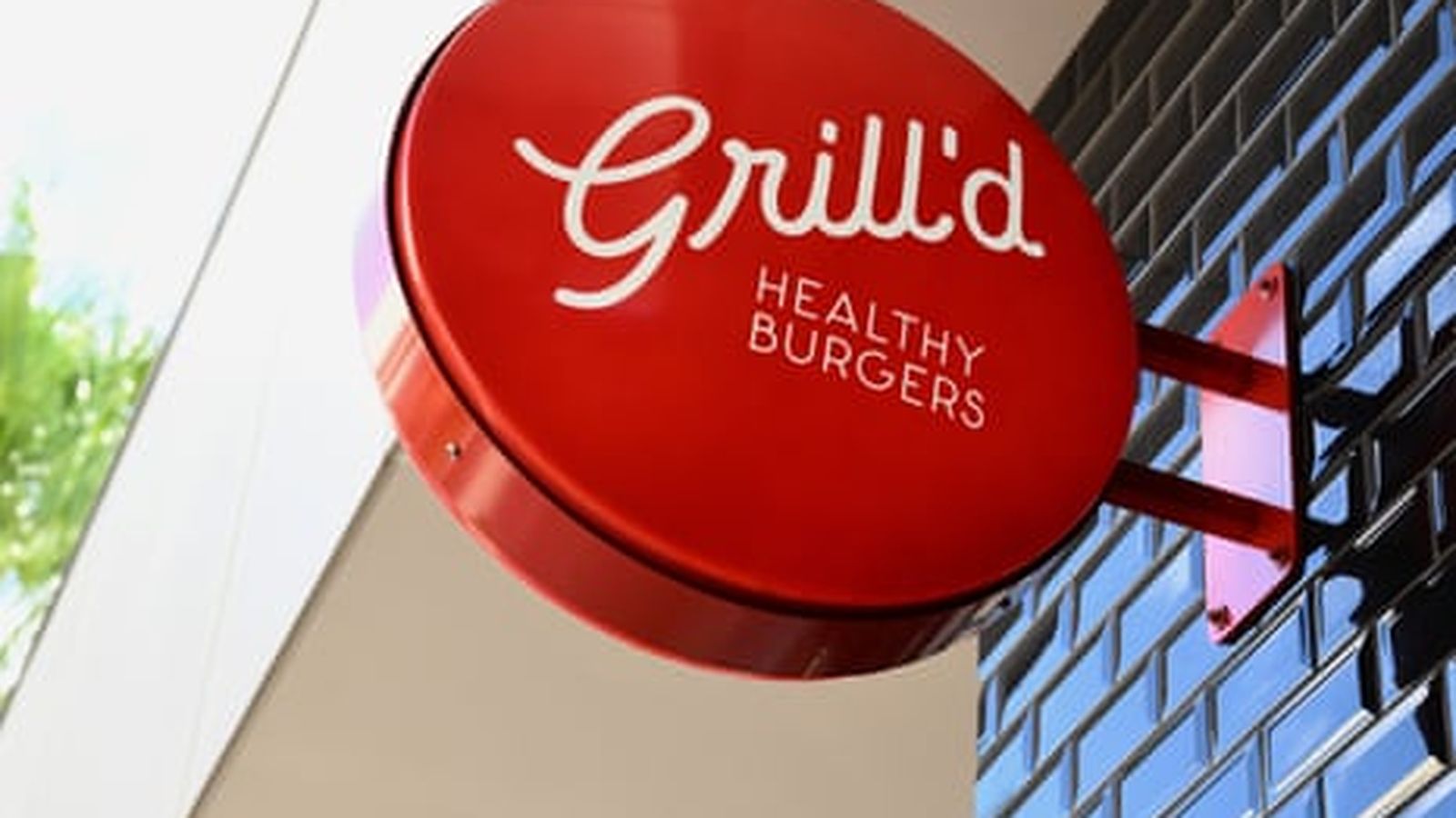 A round red Grilld healthy burgers sign mounted on a black tiled wall