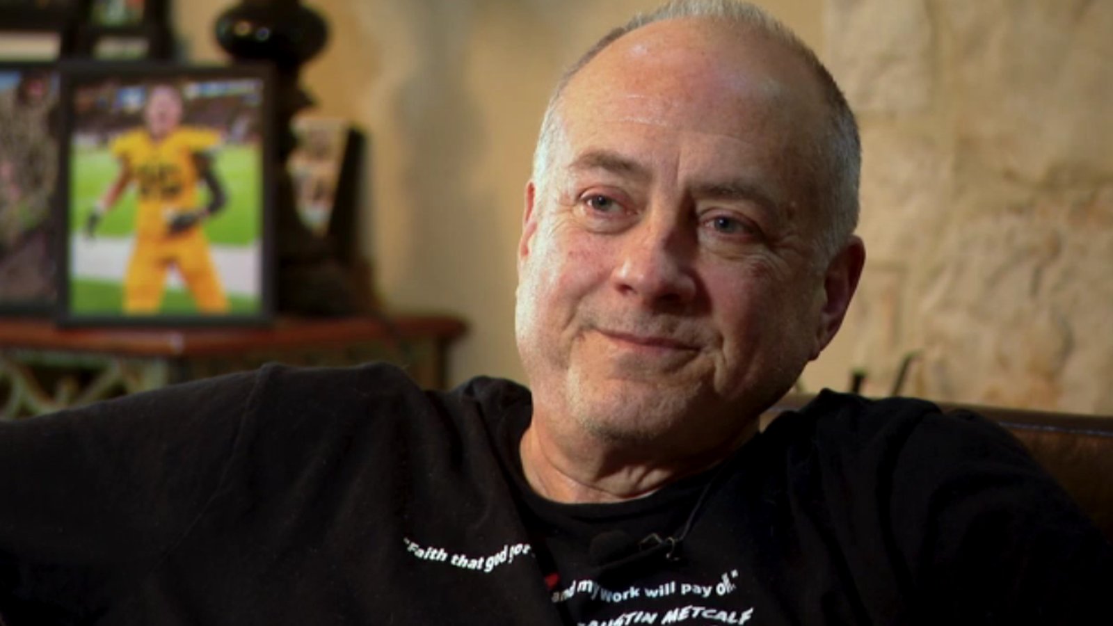 Jeff Metcalf sitting for an interview with framed photos of his son behind him
