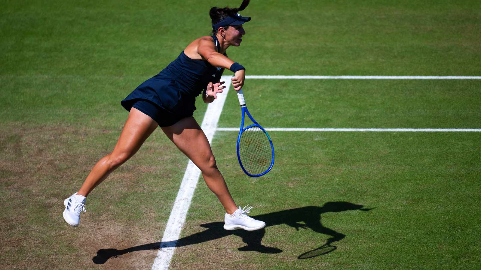 Jessica Pegula in a dark blue outfit serving on a green grass tennis court