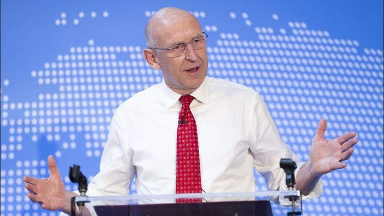 John Healey wearing a white shirt and red tie speaking at a podium