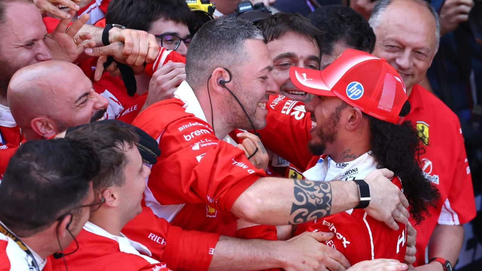 Lewis Hamilton wearing a red Ferrari cap being embraced by his team members
