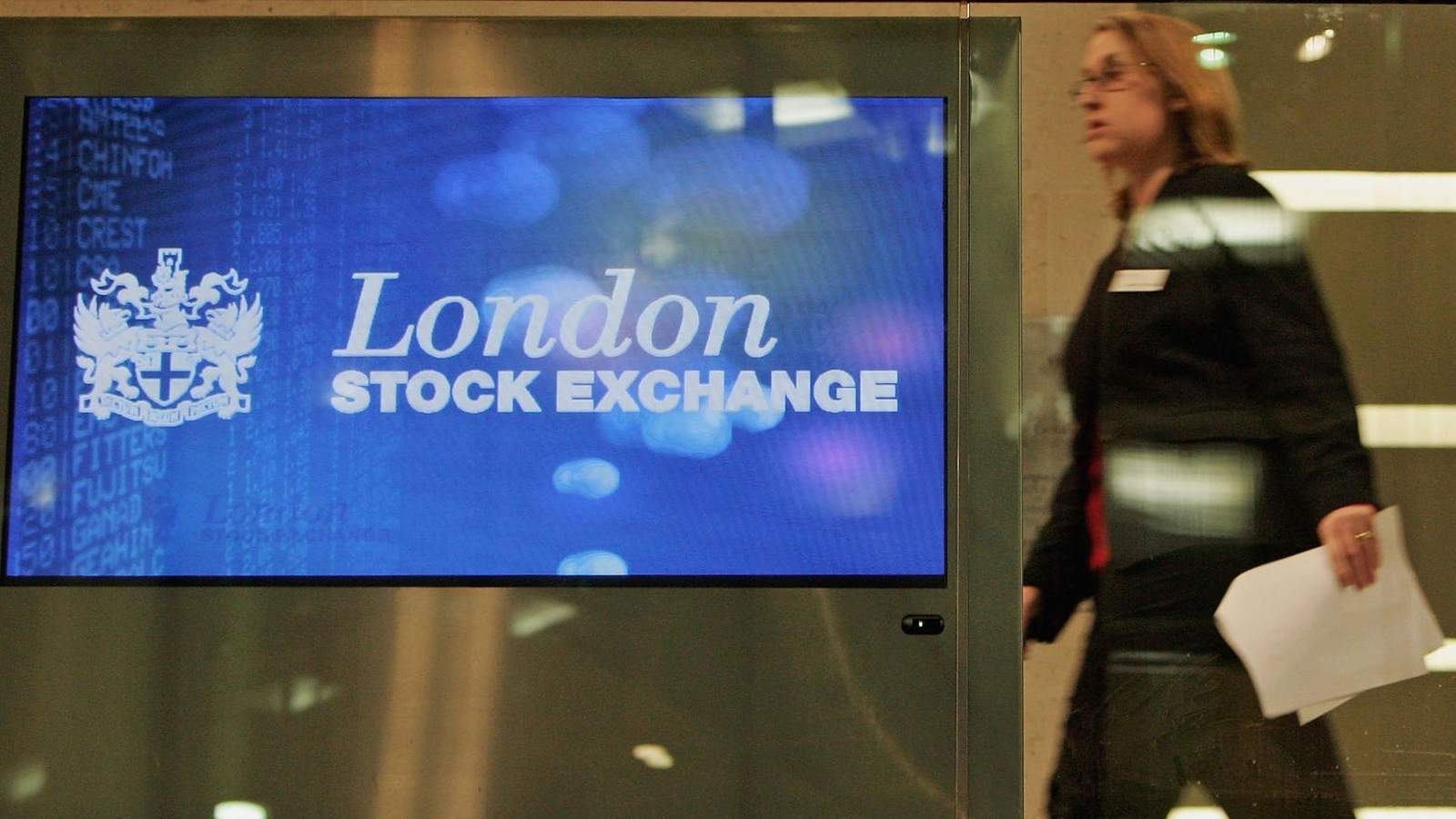 A woman walking past a digital display screen showing the London Stock Exchange logo