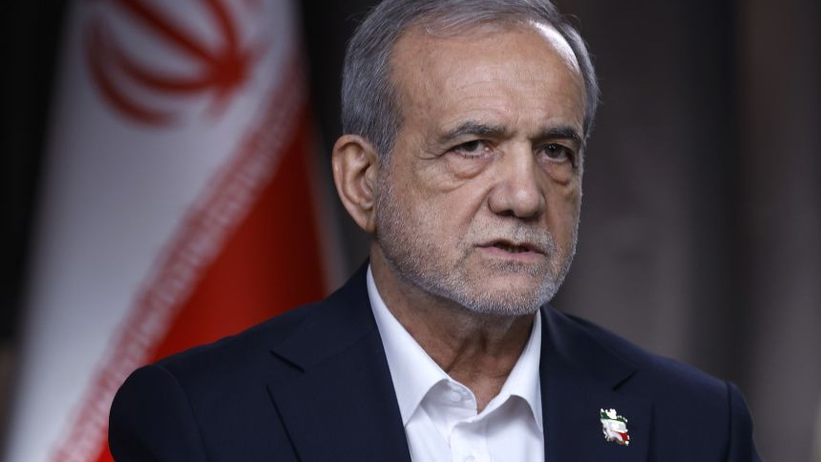 Iranian President Masoud Pezeshkian wearing a dark suit with an Iranian flag pin