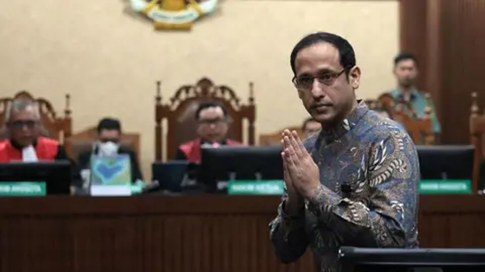 Nadiem Makarim wearing a batik shirt with hands pressed together in a courtroom