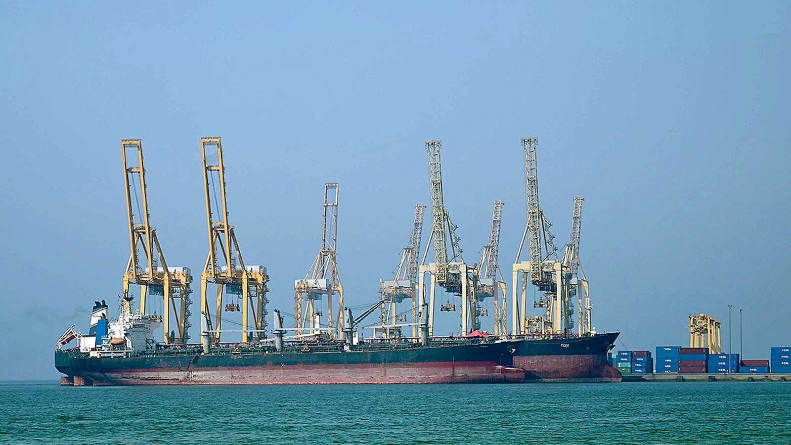 Large oil tanker ship docked at a busy industrial container port terminal