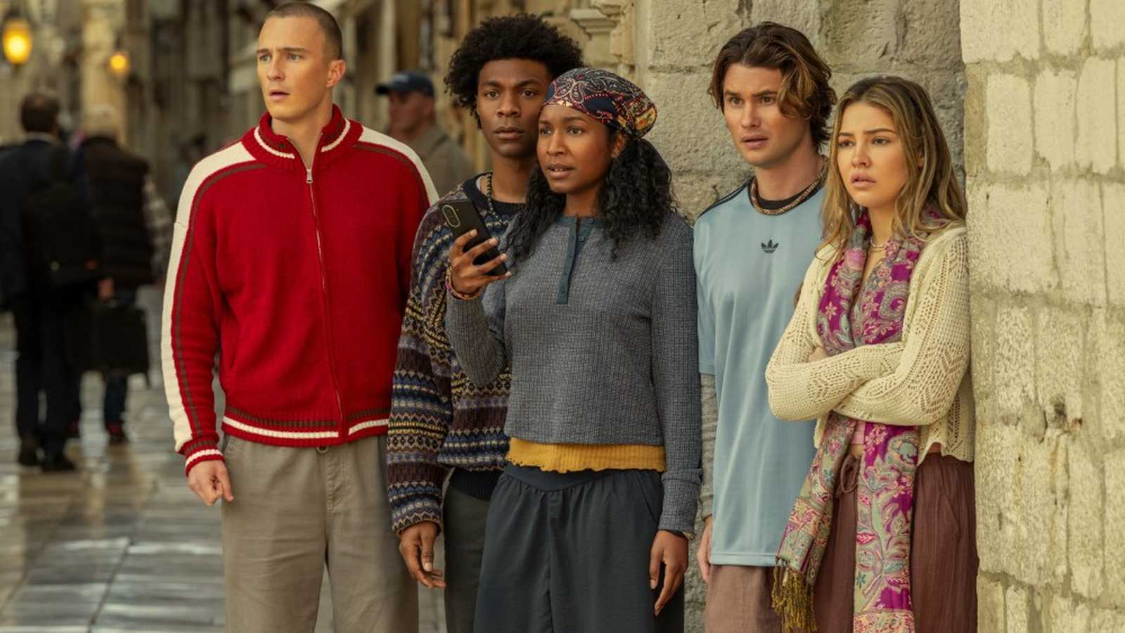 The main cast of Outer Banks standing together looking concerned in a street scene