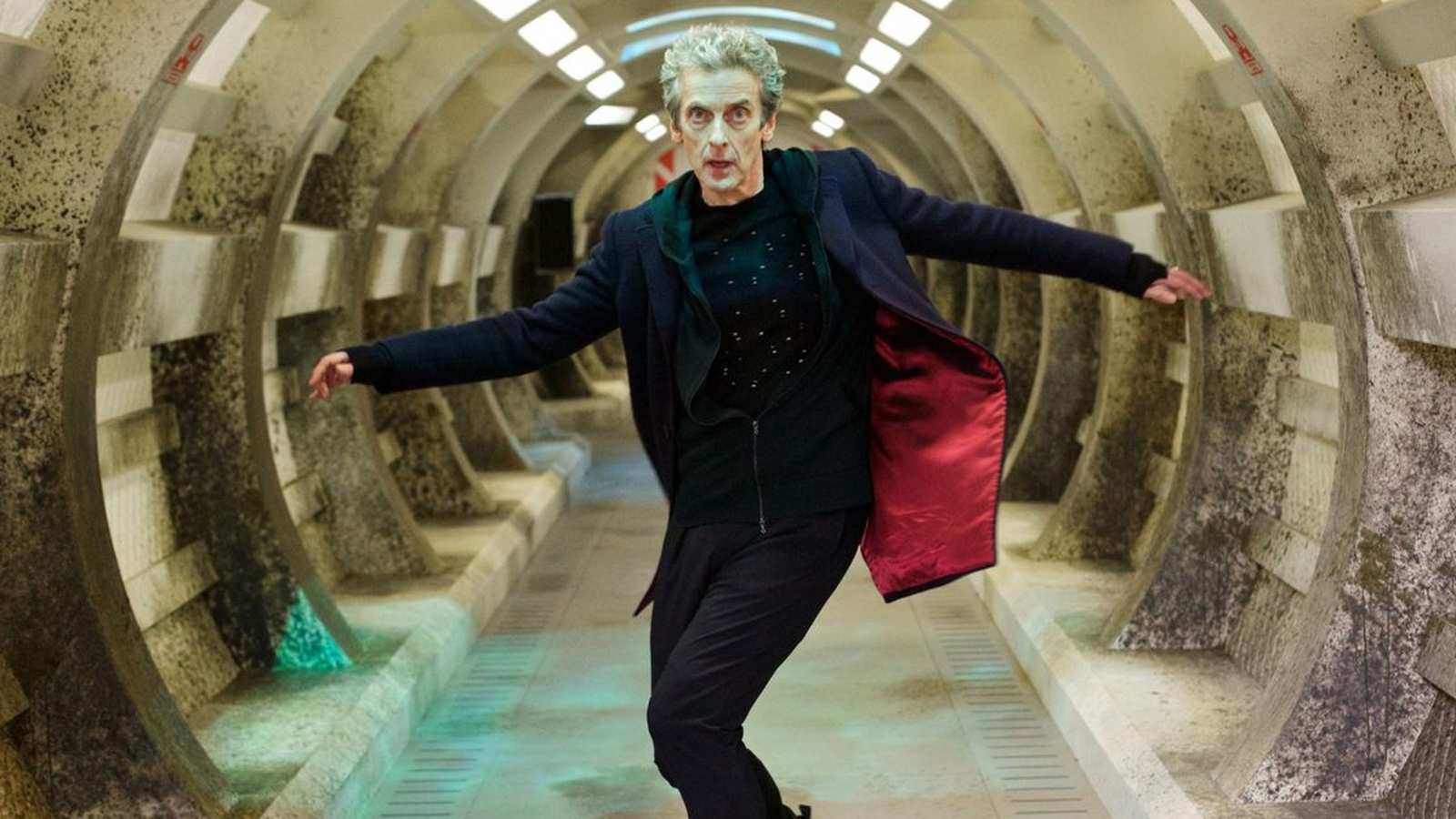Peter Capaldi standing in a futuristic tunnel wearing his dark Doctor Who coat