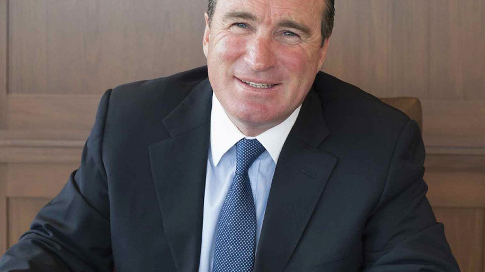 Portrait of Peter Fox wearing a dark suit and blue tie against wood paneling